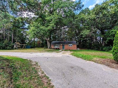 Gravel driveway leading up to the brick ranch through the trees